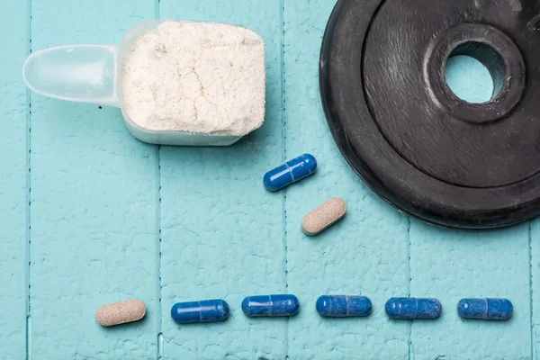 Container of milk whey protein and pills. Close-up. Blue background