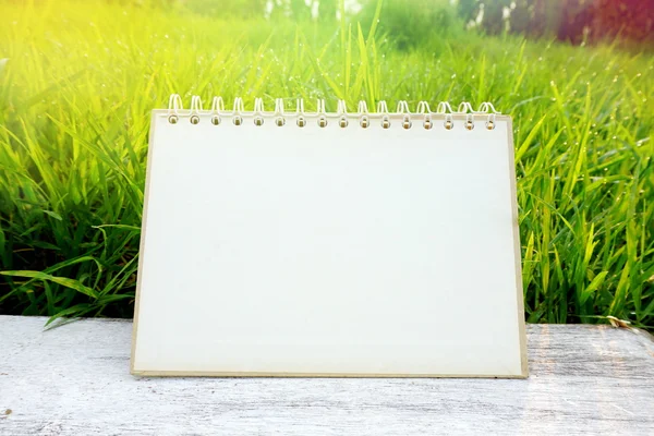 Blank paper calendar page on white wooden table over nature green field grass