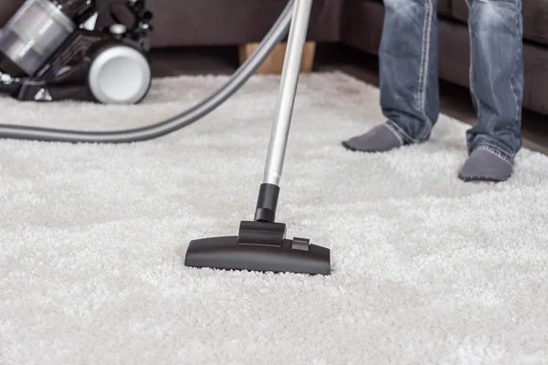 A man cleans the carpet with a vacuum cleaner.