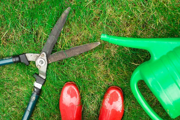 Gardening tools, red garden shoes, secateurs,  watering can on the grass,  close up.