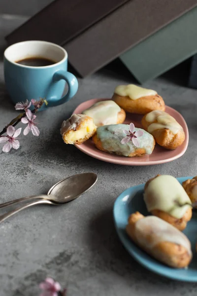 Profiteroles with butter cream and topping on the plate against grey background. Coffee break pause. Pastel shades.