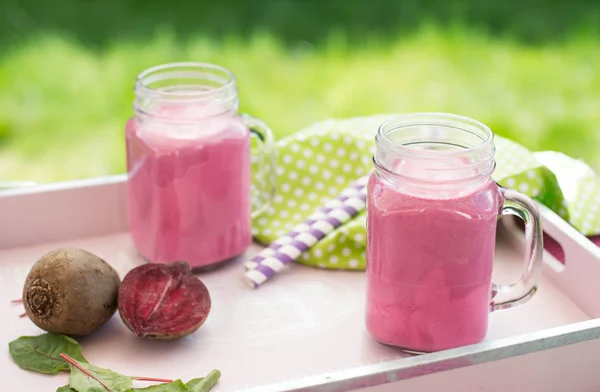 Freshly squeezed beet smoothie in a jar with a straw and ingredients.