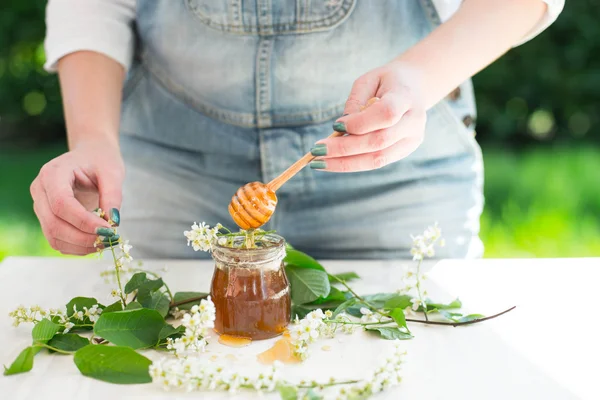 Honey dripping from a wooden honey dipper in a jar. Female hands holding honey dipper.