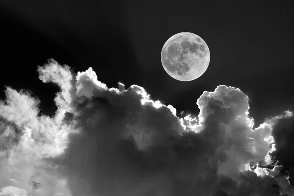 Black and white of full moon in night sky with dreamy moonlit clouds