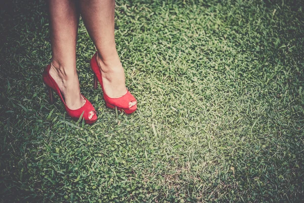 Womans legs in bright red shoes with high heels crossed on grass