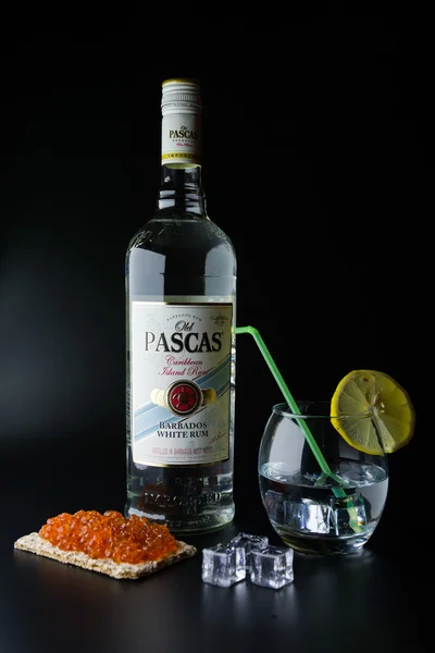 TIRASPOL, MOLDOVA - JUNE 5, 2016: Caribbean white rum bottles Old Pascas on a black background with red caviar toast with a glass of ice and a slice Lemon.