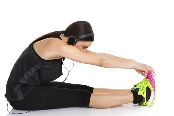 Beautiful fit caucasian lady with headphones stretching legs, arms and back.