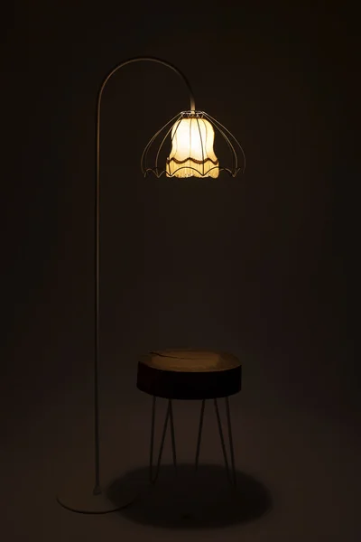 Floor lamp lit in the darkness with stool alone