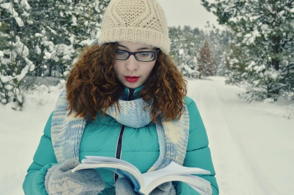 Beautiful,young,curly girl,dressed in a jacket, knitted hat, knitted scarf,reads thoughtfully book in the Park
