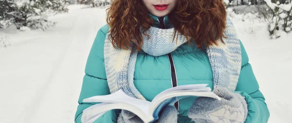 Dark-haired girl dressed in a turquoise jacket,bodily woolly hat, and a light blue scarf,reading a book in the Park,drinking tea,coffee,cocoa