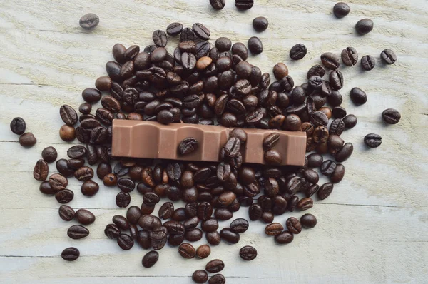 Bar of dark chocolate, milk chocolate bar, coffee beans, star anise, cinnamon sticks, seasonings, spices, close-up on a white wooden background