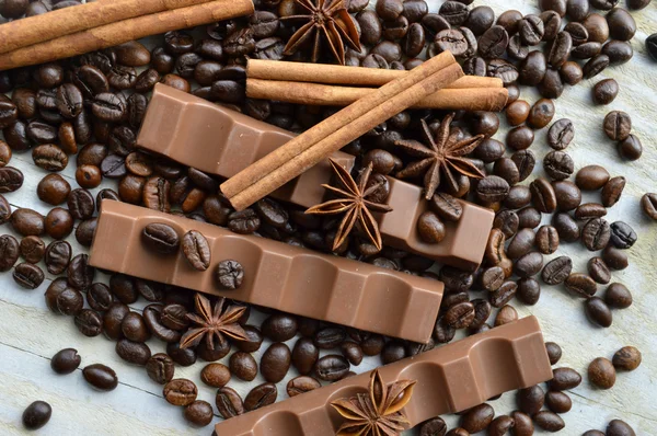 Bar of dark chocolate, milk chocolate bar, coffee beans, star anise, cinnamon sticks, seasonings, spices, close-up on a white wooden background