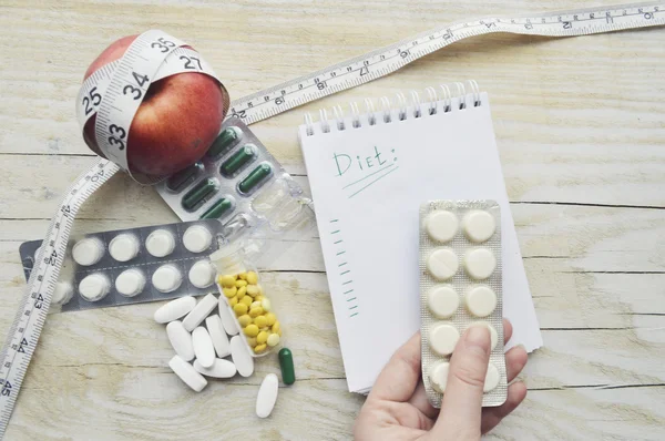 Hand with pills, notebook, apple and measuring tape