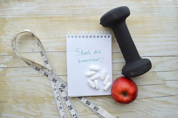 Dumbell with measuring tape and apple with pills and note pad