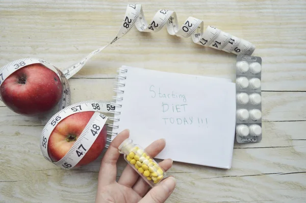 Hand with pills, notebook with two apples and measuring tape