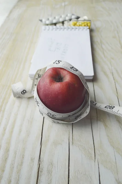 Notebook with apple, pills and measuring tape
