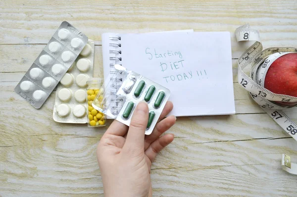 Hand with pills, notebook with apple and measuring tape