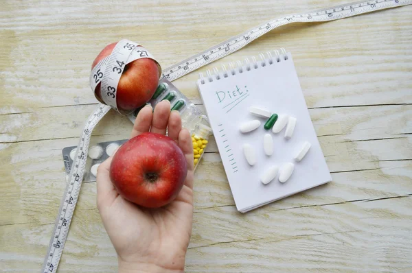 Hand with apple, measuring tape, pills and notebook