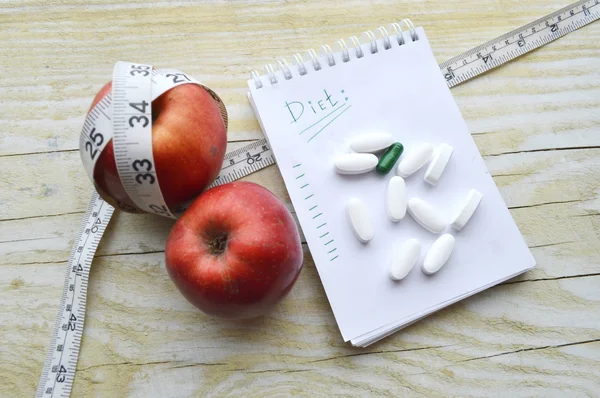 Two apples, measuring tape, pills and notebook