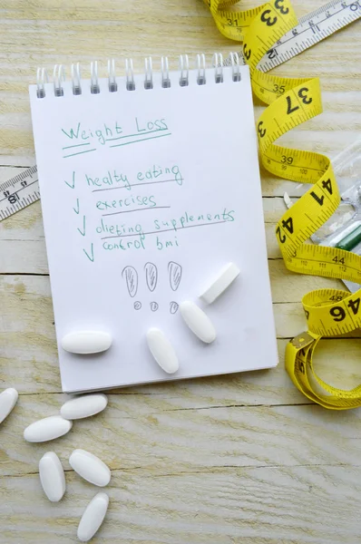 Notebook with diet plan and a measuring tape with pills
