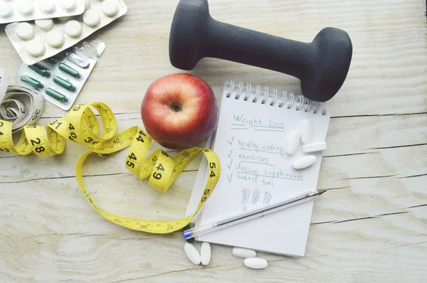 Measuring tape, pills, apple and notebook with dumbbell