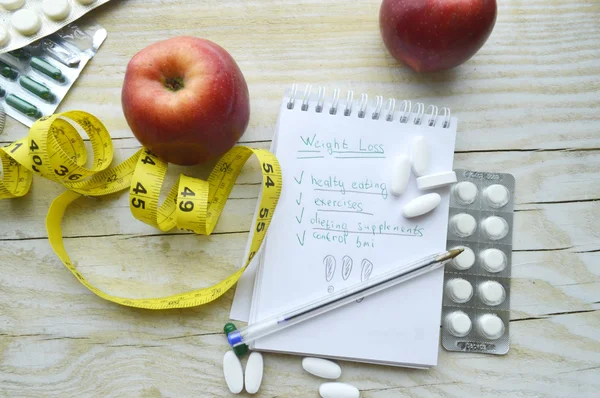 Measuring tape, pills, apples and notebook
