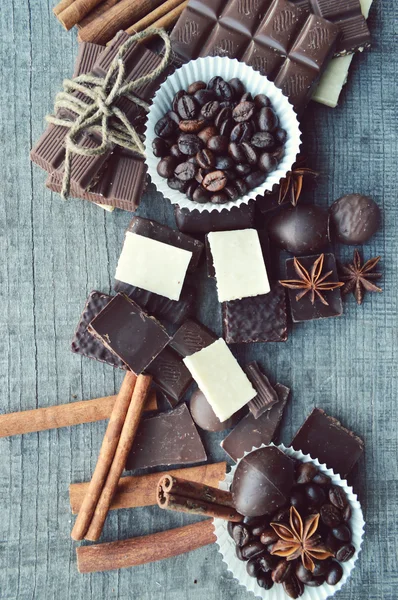 Bar of chocolate, coffee beans, hazelnuts, walnuts, cinnamon, coriander, spices .chocolate bar, candy bars,  different chocolate sweets on a wooden background
