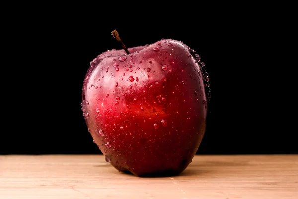 One red apple with water drops reflecting light on wooden table