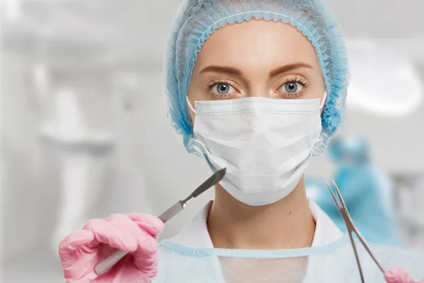 Young woman doctor with scalpel and scissors in surgery room interior