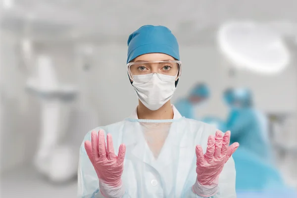 Close-up portrait of serious nurse or doctor in white mask. Looking confident and professional. Operation in the background