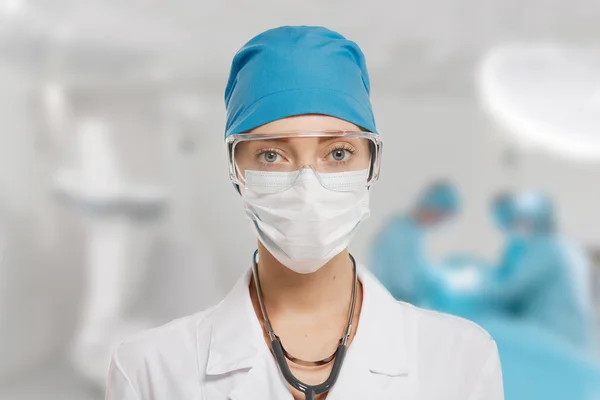 Close-up of surgeon woman looking at camera with colleagues performing in background in operation room