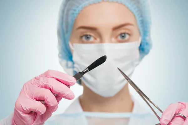 Portrait of female surgeon wearing surgical scrubs, gloves and a scrub cap, holding a surgical scalpel in her hand