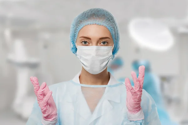 Close-up portrait of serious nurse or doctor in white mask. Looking confident and professional. Operation in the background