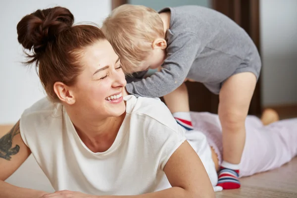 Young mother with her one years old little son dressed in pajamas are relaxing and playing in the bedroom at the weekend together, lazy morning, warm and cozy scene. Selective focus.