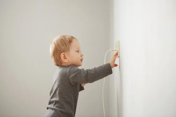 Curious little boy playing with electric plug. Trying to insert it into the electric socket. Danger at home