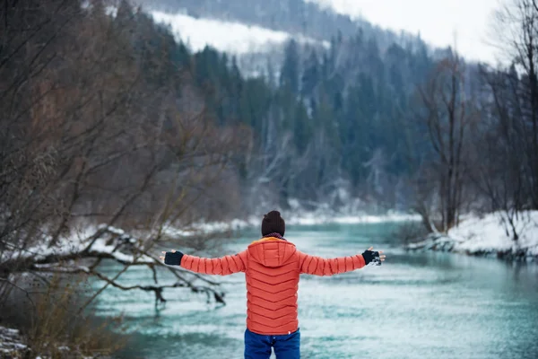 Man on solo camping trip. Winter gear walking along fast flowing rocky river, in scenic outdoor nature destination