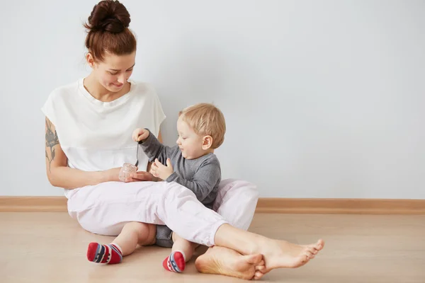 Young attractive mother with her one years old little son dressed in pajamas  giving him his first fruit smoothies food in the bedroom at the weekend together, lazy morning. Selective focus