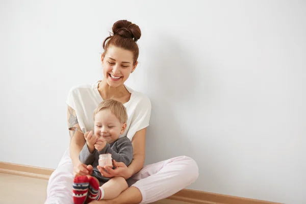 Young attractive mother with her one years old little son dressed in pajamas  giving him his first fruit smoothies food in the bedroom at the weekend together, lazy morning. Selective focus