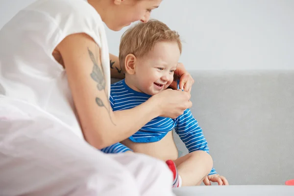 Young mother with her one years old little son dressed in pajamas are relaxing and playing in the bedroom at the weekend together, lazy morning, warm and cozy scene. Selective focus.