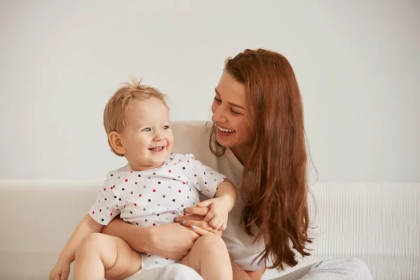 Young mother with her one years old little son dressed in pajamas are relaxing and playing in the bedroom at the weekend together, lazy morning, warm and cozy scene. Selective focus.