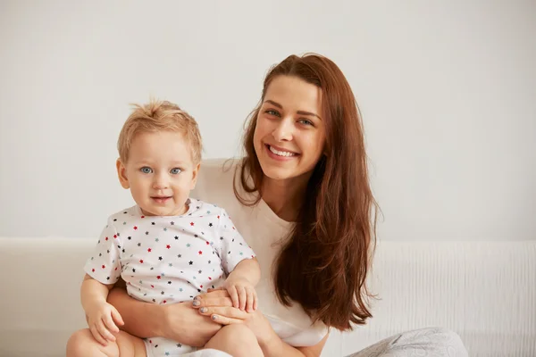 Young mother with her one years old little son dressed in pajamas are relaxing and playing in the bedroom at the weekend together, lazy morning, warm and cozy scene. Selective focus.