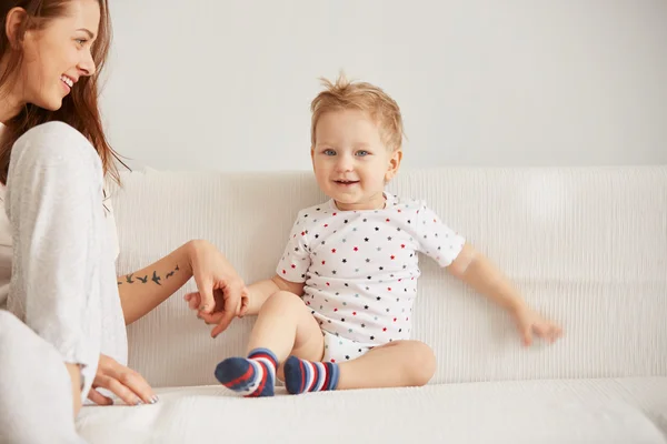 Young mother with her one years old little son dressed in pajamas are relaxing and playing in the bedroom at the weekend together, lazy morning, warm and cozy scene. Selective focus.