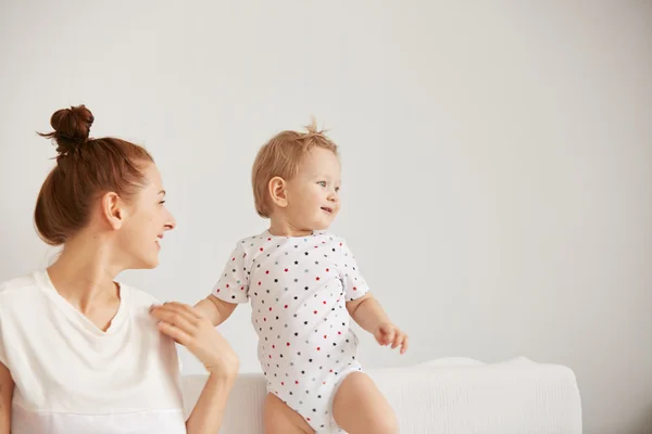 Young mother with her one years old little son dressed in pajamas are relaxing and playing in the bedroom at the weekend together, lazy morning, warm and cozy scene. Selective focus.