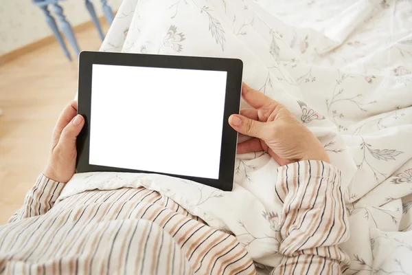 Close up to view mature woman\'s hands hold black tablet with empty screen, female hands holding touch screen tablet pc with blanc screen lying on her bed in a bedroom.