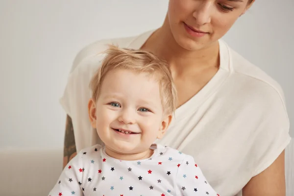 Young mother with her one years old little son dressed in pajamas are relaxing and playing in the bedroom at the weekend together, lazy morning, warm and cozy scene. Selective focus.