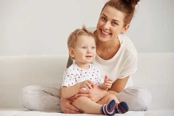 Young mother with her one years old little son dressed in pajamas are relaxing and playing in the bedroom at the weekend together, lazy morning, warm and cozy scene. Selective focus.