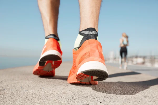 Sports background. Athlete runner feet running on road closeup on shoe. Man fitness jog workout wellness concept. Man runner legs and shoes in action on road outdoors at road near sea.