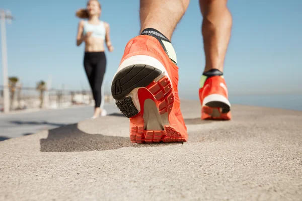 Sports background. Athlete runner feet running on road closeup on shoe. Man fitness jog workout wellness concept. Man runner legs and shoes in action on road outdoors at road near sea.