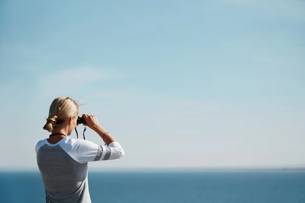 Woman tourist looking through binoculars at distant sea, enjoying landscape, copy space for your text