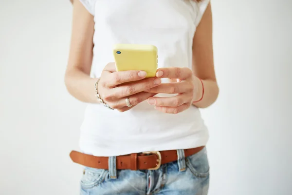 Selective focus. Close up view of woman\'s hands typing on mobile phone. Isolated shot of female wearing white sleeveless T-shirt and jeans reading news on cell phone while browsing Internet at home.